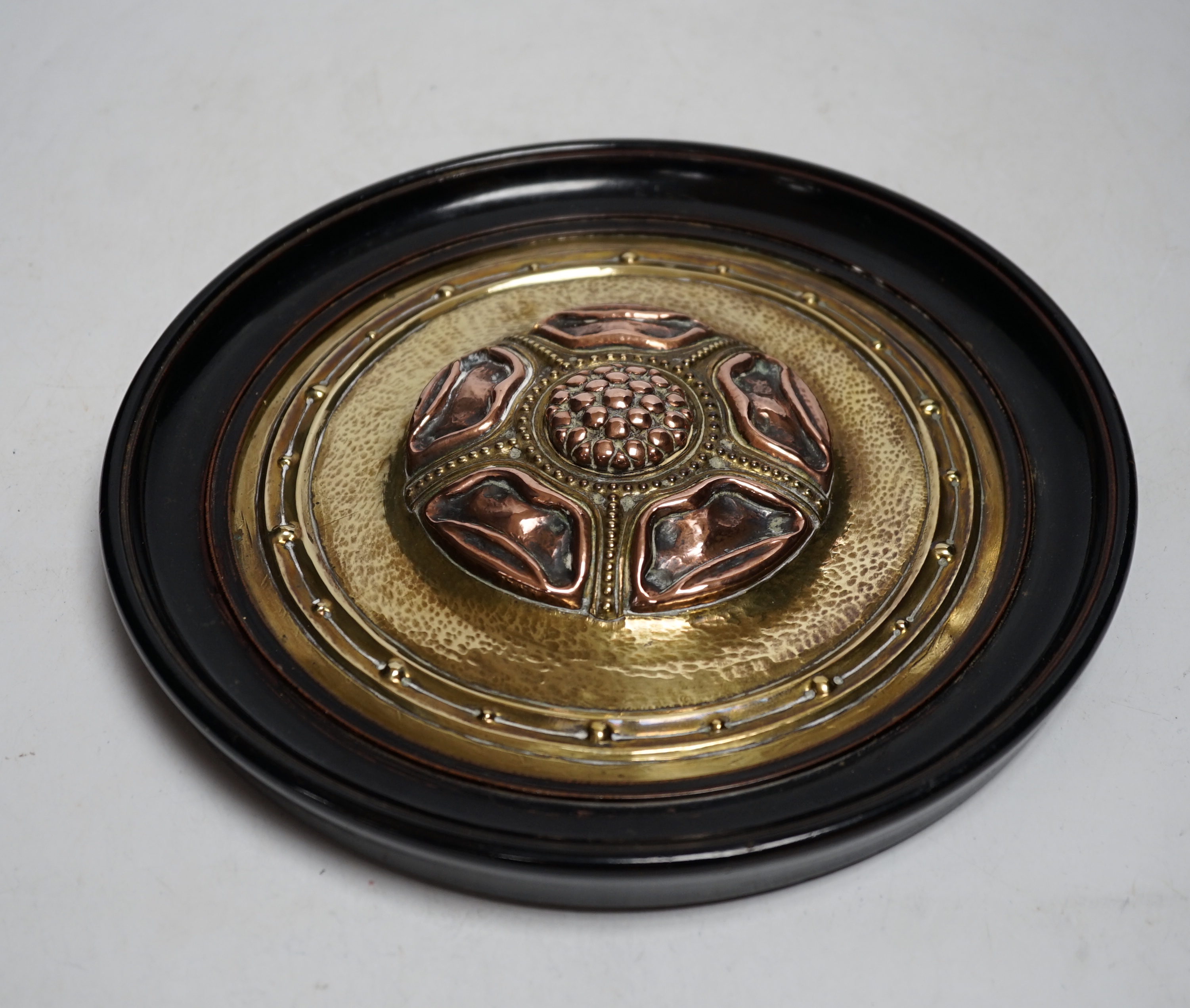 An Arts and Crafts brass and copper roundel, in the manner of Archibald Knox, monogrammed CA, ebony framed, overall 27cm